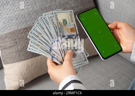 Uno smartphone con schermo cromato verde e molte banconote da cento dollari nelle mani Foto Stock