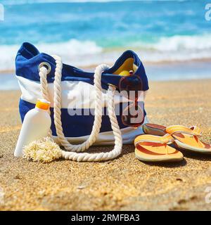Borsa da spiaggia, infradito, bottiglia di crema solare e occhiali da sole su una spiaggia balinese Foto Stock