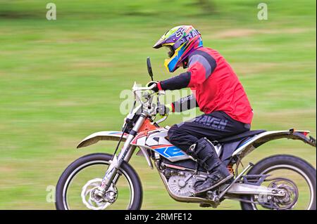 Uomo di mezza età durante un giro di hobby sul suo cortile su una moto elettrica KTM da motocross su un campo. Foto in stile panoramica. Taglio dinamico. repubblica Ceca. Foto Stock