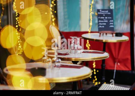 Accogliente caffetteria parigina all'aperto con luci gialle e menu a tavola, con attenzione agli occhiali Foto Stock