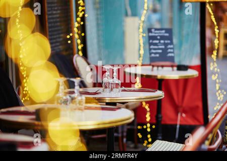 Accogliente caffetteria parigina all'aperto con luci gialle e menu a tavola, con attenzione agli occhiali Foto Stock