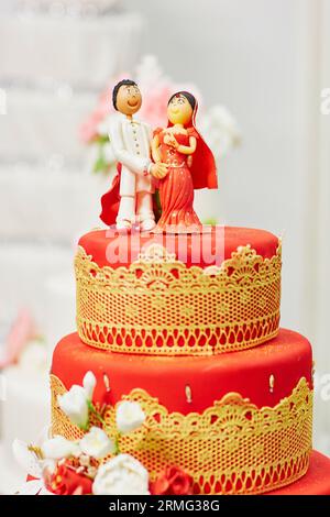Splendida torta nuziale rossa e gialla in stile indiano con statuette per sposi e sposi in cima Foto Stock