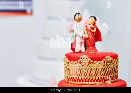 Splendida torta nuziale rossa e gialla in stile indiano con statuette per sposi e sposi in cima Foto Stock