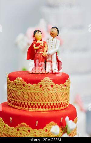 Splendida torta nuziale rossa e gialla in stile indiano con statuette per sposi e sposi in cima Foto Stock