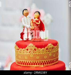 Splendida torta nuziale rossa e gialla in stile indiano con statuette per sposi e sposi in cima Foto Stock