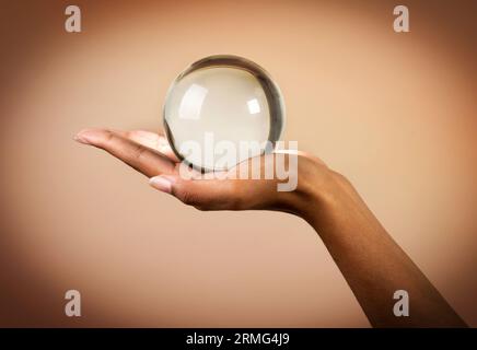 Coltiva la mano non riconoscibile di una donna afroamericana che tiene la sfera di cristallo su sfondo beige Foto Stock