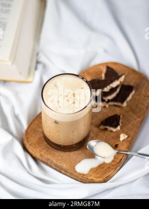 Un primo piano di un caffellatte freddo in un bicchiere su un asse di legno sulle lenzuola bianche Foto Stock