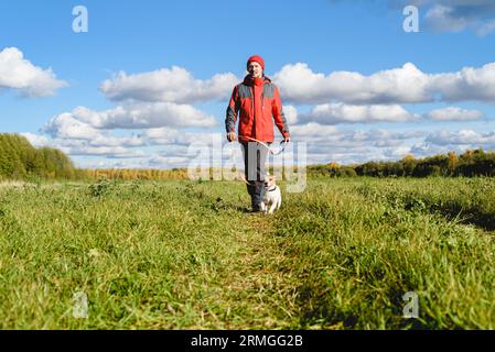 Uomo e cane al guinzaglio camminano lungo il sentiero attraverso il prato in una luminosa giornata autunnale Foto Stock