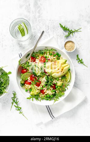 Insalata di couscous con broccoli, piselli verdi, pomodori, avocado e rucola fresca. Cibo vegetariano a base vegetale naturale sano per pranzo, cucina israeliana, Foto Stock