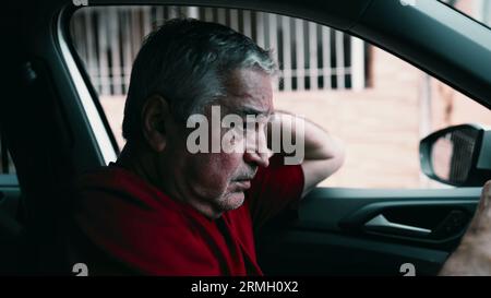 Un uomo anziano che soffre di dolore emotivo in auto, parcheggiato in strada. Drammatica persona anziana solitaria in circostanze disperate e terribili, che lotta in quiete Foto Stock