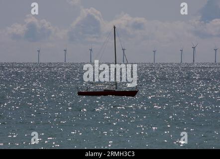 Una barca a vela ancorata al largo di Shoreham con il parco eolico offshore Raviera sul retro Foto Stock