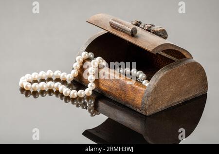 Vecchia scatola di legno con collana di perle su sfondo nero a specchio. Foto Stock