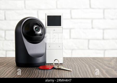 Concetto di apparecchiature di sicurezza domestica e di sicurezza. Telecamera Web IP con telecomando e tasti di casa sul tavolo all'interno della stanza Foto Stock