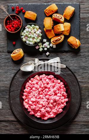 insalata cremosa di mirtilli rossi con mini marshmallow, mela fresca e noci pecan in ciotola nera su tavolo di legno scuro con dolci alla cannella, ricetta americana, verdura Foto Stock