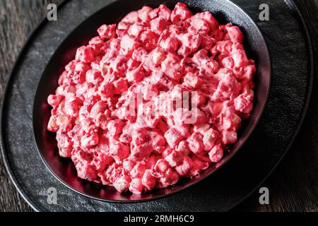 insalata cremosa di mirtilli rossi con mini marshmallow, mela fresca e noci pecan in ciotola nera su tavolo di legno scuro, primo piano Foto Stock