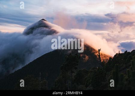 Nuvola vola sopra la cima del vulcano Fuego in Guatemala, creando una scena serale drammatica Foto Stock