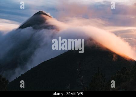 Nuvola vola sopra la cima del vulcano Fuego in Guatemala, creando una scena serale drammatica Foto Stock