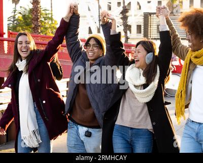 Gruppo di giovani multietnici in abiti invernali che si divertono a camminare con le mani unite in una città Foto Stock