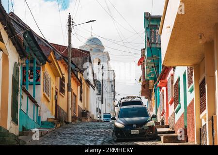 Una strada di ciottoli vuota nella città vecchia di Flores, situata su un'isola nel lago Petén Itzá, Guatemala. Cattedrale di nostra Signora di Los Remedios vista dietro. Foto Stock