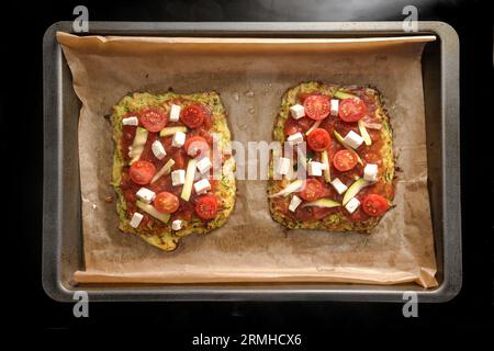 Pizza vegetariana a pezzetti su una crosta di zucchine e fiocchi d'avena, condita con pomodori e feta su un vassoio con carta da forno, sano e basso contenuto di carboidrati Foto Stock