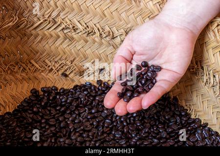 la mano di una donna bianca che mostra i chicchi di caffè tostati da lei che si trovano all'interno di un cestino di esparto, per poi macinarli. fotografia di paesaggi Foto Stock