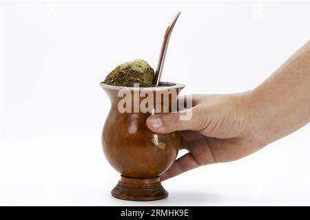 Mano che regge una tazza di compagno, chiamata chimarrão, dal Sud America. Sfondo bianco isolato, utensili yerba mate, ciotola brasiliana. Tipico drink da Foto Stock