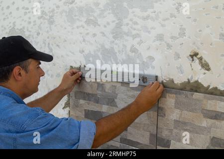 Immagine di una piastrella che utilizza una livella per controllare la posa di piastrelle su una parete. Lavori di ristrutturazione fai da te. Foto Stock