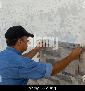 Immagine di una piastrella che utilizza una livella per controllare la posa di piastrelle su una parete. Lavori di ristrutturazione fai da te. Foto Stock