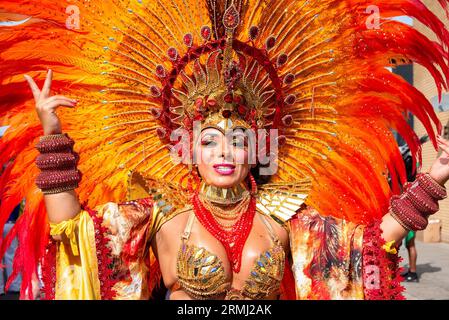 Una bellissima ballerina di samba vista in posa per una foto prima della sfilata in una colorata corona di piume di carnevale. Il Carnevale di Notting Hill è uno dei più grandi festival di strada del mondo. È iniziato nel 1966, ma ha avuto origine con il Carnevale caraibico organizzato nel 1959 con la comunità di immigrati da Trinidad e Tobago. Quest'anno il Carnevale di Notting Hill segna il 50° anniversario dell'introduzione dei sistemi audio e delle band Mas. Inoltre segna il 75° anniversario dell'arrivo dei passeggeri dell'Empire Windrush nel Regno Unito. Foto Stock