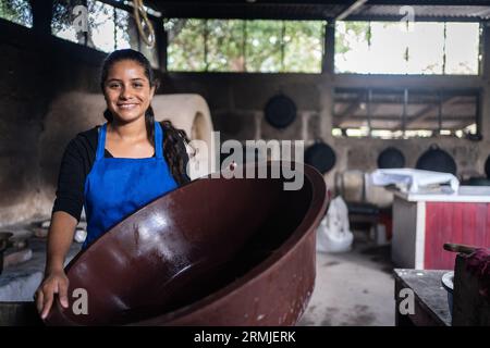 Donna latina con un grande contenitore per lavare i piatti in una cucina povera Foto Stock