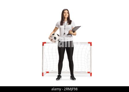 Allenatore di calcio femminile con un fischio che tiene una clipboard e una palla davanti a un mini goal isolato su sfondo bianco Foto Stock
