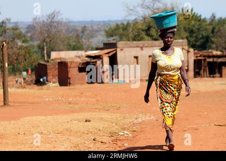 Una donna che bilancia un piatto di plastica sulla testa mentre cammina verso un punto d'acqua a Malingunde, Lilongwe, Malawi. Foto Stock