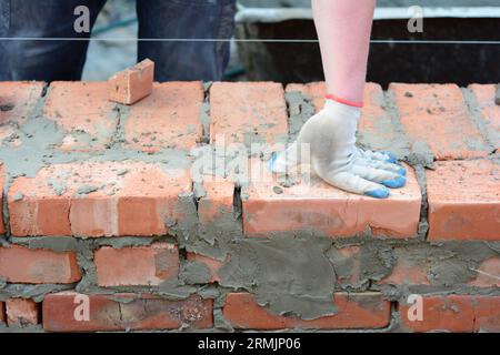 Un muratore sta costruendo un muro di casa in mattoni. Primo piano su metà pipistrello e quarto mattone sulla costruzione del muro di mattoni della casa. Foto Stock