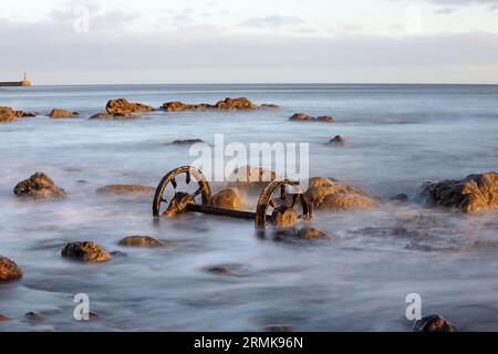 Old chaldron Wagon Wheels sulla spiaggia chimica con il faro di Seaham Harbour Beyond, Durham Heritage Coast, Seaham, County Durham, Regno Unito Foto Stock