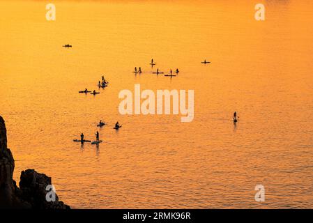 Le persone avventurose su una tavola da paddle stand up stanno pagaiando durante una luminosa e vibrante alba Foto Stock