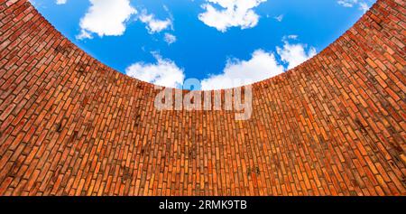 Una struttura a parete circolare in mattoni con un cielo blu con nuvole bianche sullo sfondo Foto Stock