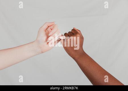 Primo piano con le belle mani scure delle donne che rendono pinkie promettente sullo sfondo grigio Foto Stock