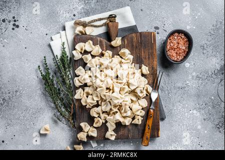 Manti non cotti su tavola di legno con erbe, cibo crudo. Sfondo grigio. Vista dall'alto. Foto Stock