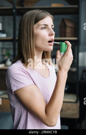 Vista laterale giovane donna che utilizza spray per gola Foto Stock