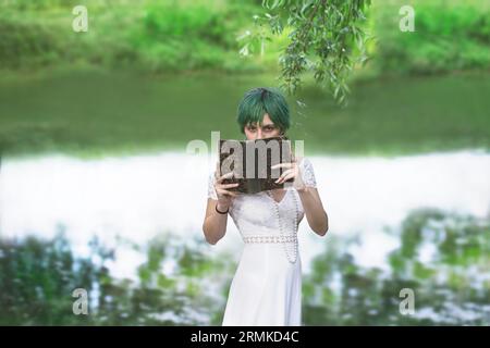 misteriosa ragazza che mostra il suo volto nascosto da un libro in mezzo alla natura Foto Stock