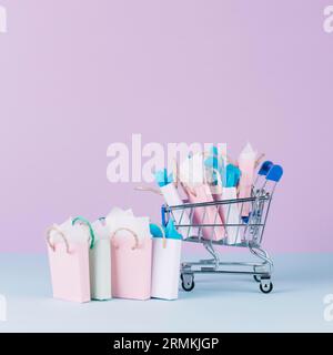 Carrello in miniatura pieno di sacchetti di carta per la spesa, sfondo rosa anteriore Foto Stock