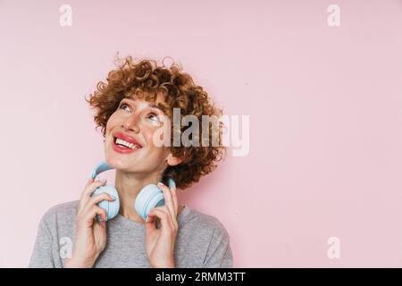 Zenzero maturo con cuffie che guardano lontano lo spazio di copia isolato su sfondo rosa Foto Stock