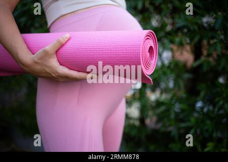 una giovane donna incinta tiene in mano un tappetino da yoga rosa. primo piano Foto Stock