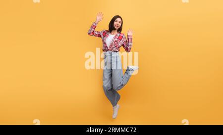 Gioiosa giovane donna asiatica che salta in aria e sorride alla macchina fotografica, eccitata donna che si diverte, a tutta lunghezza, spazio per copiare Foto Stock