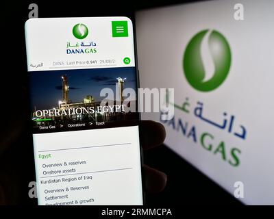 Persona che possiede uno smartphone con la pagina Web dell'azienda petrolifera degli Emirati Dana gas PJSC sullo schermo davanti al logo. Concentrarsi sul centro del display del telefono. Foto Stock