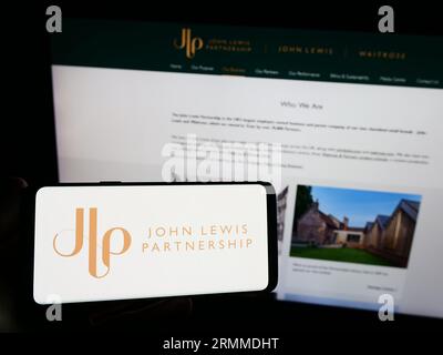 Persona che possiede uno smartphone con il logo della società di vendita al dettaglio John Lewis Partnership plc sullo schermo di fronte al sito Web. Concentrarsi sul display del telefono. Foto Stock