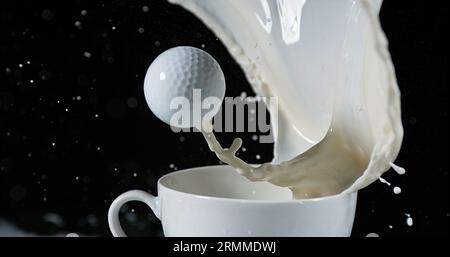 Pallina da golf in una ciotola con latte esplosivo su sfondo nero Foto Stock