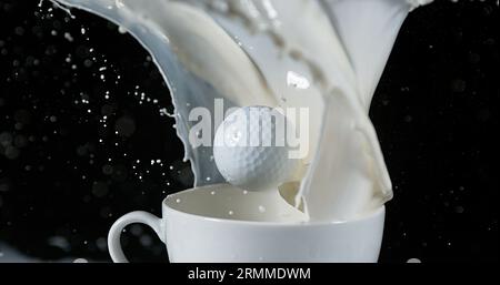 Pallina da golf in una ciotola con latte esplosivo su sfondo nero Foto Stock