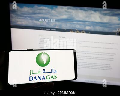 Persona che possiede uno smartphone con il logo della società petrolifera degli Emirati Dana gas PJSC sullo schermo di fronte al sito Web. Concentrarsi sul display del telefono. Foto Stock