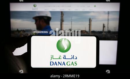 Persona in possesso di un cellulare con il logo della società petrolifera degli Emirati Dana gas PJSC sullo schermo davanti alla pagina Web aziendale. Concentrarsi sul display del telefono. Foto Stock